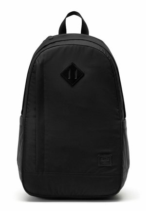 Sac à dos en tissu noir avec poignée supérieure, forme arrondie, pièce en cuir en forme de losange à l'avant et petite étiquette de marque rectangulaire près du bas.