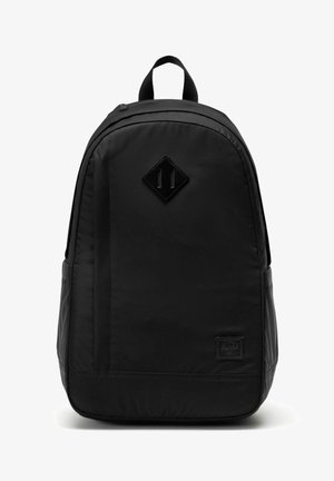 Sac à dos en tissu noir avec poignée supérieure, forme arrondie, pièce en cuir en forme de losange à l'avant et petite étiquette de marque rectangulaire près du bas.