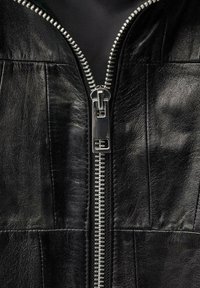 Crna kožna jakna s vertikalnim zatvaračem s metalnim detaljima, kviltanom teksturom i šivanim detaljima duž prednje strane.