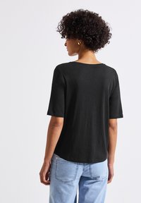 Černé bavlněné tričko s kulatým výstřihem a krátkými rukávy, z pohledu ze zad, v kombinaci se světle modrými džíny.