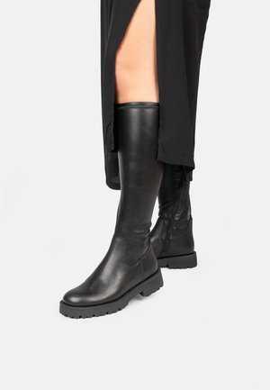 Knee-high black leather boots with textured finish, round toe, thick rubber sole, side zipper, and minimalistic design.