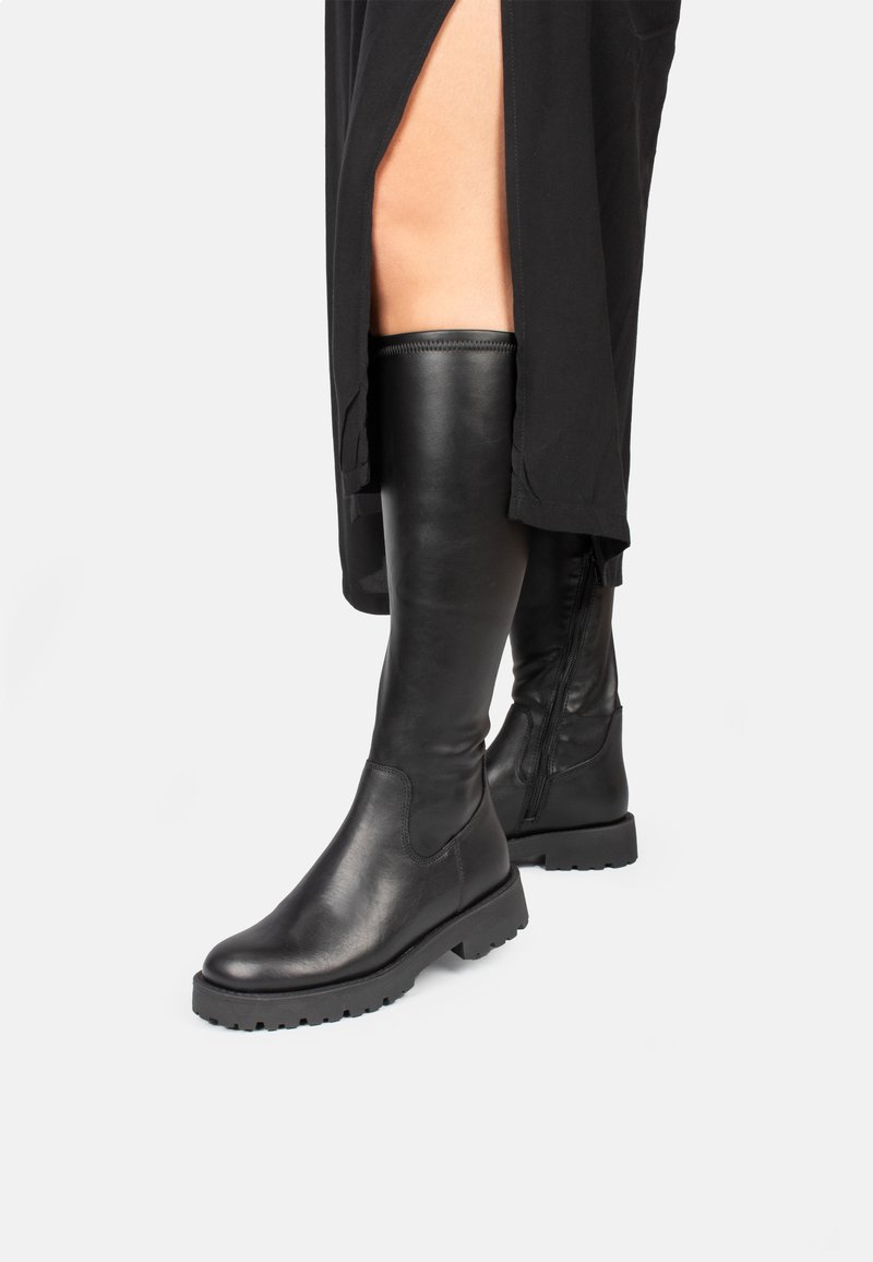 Botas de cuero negras hasta la rodilla con acabado texturizado, punta redonda, suela de goma gruesa, cremallera lateral y diseño minimalista.