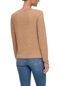 Langärmliger, hellbrauner Pullover mit Rundhals-Ausschnitt und weicher Textur, kombiniert mit blauen Jeans aus Denim mit Gesäßtaschen.
