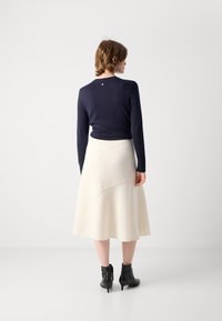Mørkeblå genser med lange ermer, kombinert med et kremfarget, kne-langt skjørt med asymmetrisk design. Svarte ankelstøvler fullfører antrekket.