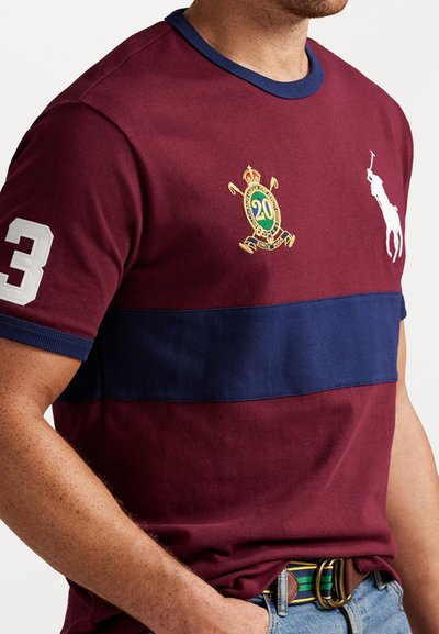 Bordo kokvilnas T-krekls ar tumši zilu horizontālu svītru, balto ciparu "3" uz piedurknes, izšūtu logotipu un polo spēlētāja grafiku.