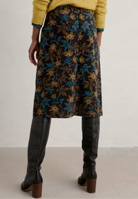 Kwiecista spódnica z czarnej tkaniny, zdobiona brązowymi i turkusowymi kwiatami. Połączona z czarnymi kozakami sięgającymi do kolan i żółtym dzianinowym swetrem.