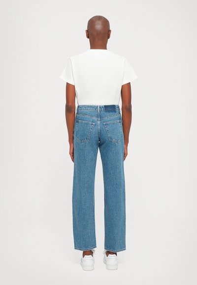 Light blue denim jeans with a straight fit, high waist, and two back pockets, paired with a plain white t-shirt and white sneakers.