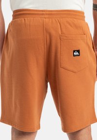 Oranžové bavlnené šortky s elastickým pásom, s bočnou vreckom a malou čiernou nášivkou. Hladká štruktúra, dĺžka po kolená.