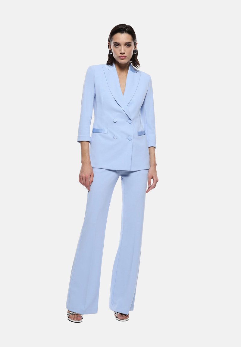 Completo su misura blu chiaro con giacca doppiopetto e pantaloni svasati. Presenta un collo a revers e sottili strisce a contrasto. Tessuto liscio.