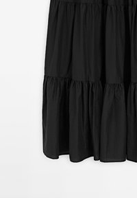 Gonna nera a strati realizzata in tessuto leggero e sgualcito. Presenta tre strati arricciati con orlo liscio. Design semplice, senza chiusure visibili.