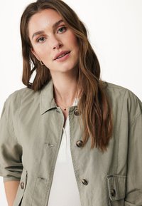 Giacca verde oliva chiaro in un tessuto morbido e testurizzato. Caratterizzata da un colletto, bottoni frontali e tasche applicate. Maniche corte.