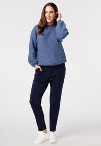 Dik blauwe gebreide trui met een ronde halslijn en ballonmouwen, gecombineerd met slim-fit marineblauwe broek en witte sneakers.