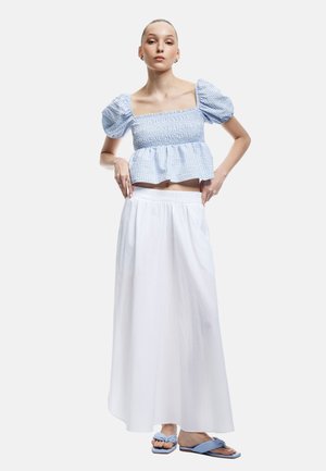 Top corto azul de cuadros de vichy con tirantes fruncidos y mangas abullonadas, combinado con una falda maxi blanca. Presenta sandalias planas azules con detalles de nudo.