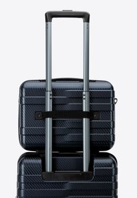 Valigia rigida di colore blu scuro con un motivo testurizzato, dotata di un manico grigio retrattile e di una cinghia nera per la stabilità.