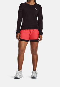 Camisa negra de manga larga combinada con pantalones cortos deportivos rojos con ribetes negros. Zapatillas de correr grises con cordones y acentos de malla.