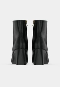 Botas de tornozelo em couro preto com um salto bloco alto, apresentando um fecho com zíper na parte de trás e uma textura suave. Design simples e elegante.