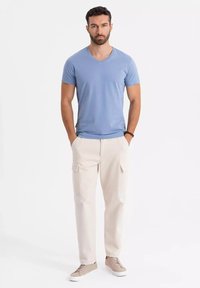 Světle modré tričko s výstřihem do V spárované s krémovými cargo kalhotami s bočními kapsami a béžovými teniskami s bílou podešví. Minimalistický design.