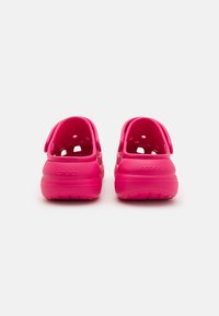 Crocs rosas con un acabado liso y brillante, vista trasera. Presentan agujeros para ventilación, correas en el talón para un ajuste seguro y suelas texturizadas.