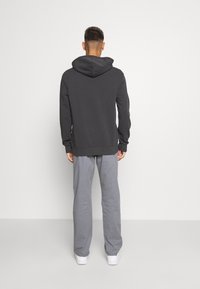 Felpa grigia scura con tasca a canguro, abbinata a pantaloni della tuta grigi chiari. Il materiale sembra morbido e confortevole, con un design casual.