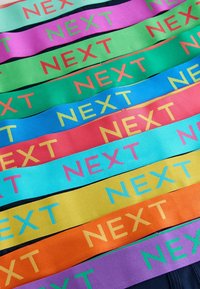 Barevné textilní pruhy s nápisem „NEXT“ potištěným kontrastními barvami. Obsahuje různé odstíny: růžovou, zelenou, modrou, oranžovou a žlutou.