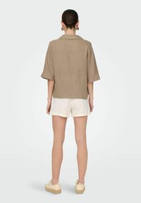 Camicia di lino marrone chiaro a maniche corte con colletto a punta. Abbinata a pantaloni corti bianchi e scarpe casual color beige. Design semplice e traspirante.
