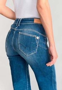 Jeans blu slim fit a vita media realizzati in denim. Presentano tasche posteriori curve, cuciture decorative e un'etichetta in pelle con il marchio sulla vita.