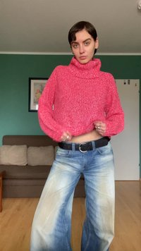 Κόκκινο πλεκτό πουλόβερ με ζιβάγκο και φαρδιά μανίκια, συνδυασμένο με ανοιχτό μπλε τζιν παντελόνι με φαρδιά καβάλο, και μαύρη ζώνη με στρογγυλή αγκράφα.