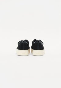 Sneaker in suede nero con suola in gomma crema a contrasto, dotate di un dettaglio posteriore liscio e di un branding sottile sul tallone.