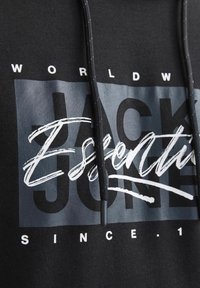 Black hoodie featuring a mix of white and gray graphics, including "JACK & JONES" and "ESSENTIAL" text, with drawstrings and a textured finish.
