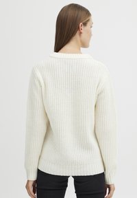 Hvit strikket genser med ribbestrikket kant og mansjetter, med en strukturert veving og en bred, avrundet halslinning. Designet er avslappet og uformelt.