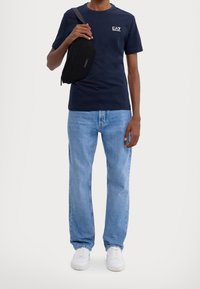 Mörkblå bomull T-shirt med vitt tryck, ljusblå jeans, svart crossbody-väska och vita sneakers. Avslappnad outfit med enkel design.