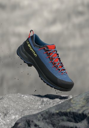 Modré a čierne turistické topánky s červenými akcentmi, vyrobené z textúrovanej syntetickej látky. Obsahujú robustnú podrážku a priedušný sieťovaný jazyk.