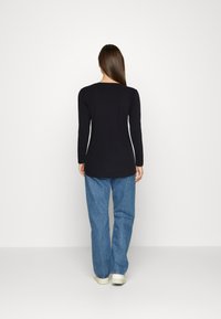 Schwarzes Langarmshirt mit Rundhalsausschnitt, kombiniert mit lockeren Jeans. Das Shirt hat einen geraden Schnitt und reicht bis unter die Hüften.