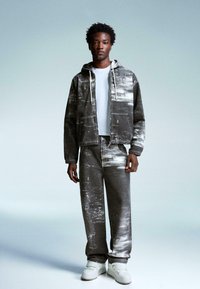 Hooded gray denim jacket with white paint splatter over a matching pair of loose jeans; paired with white sneakers and a basic white t-shirt.
