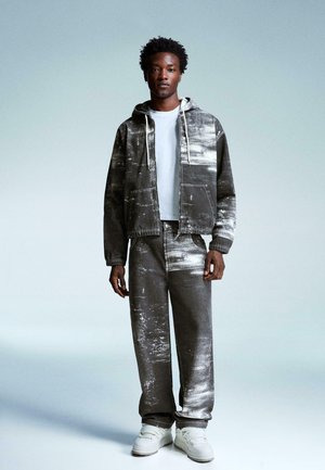 Hooded gray denim jacket with white paint splatter over a matching pair of loose jeans; paired with white sneakers and a basic white t-shirt.