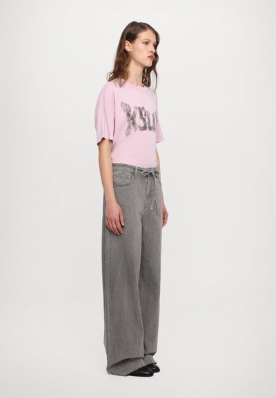 Pink short-sleeve T-shirt with black graphic text, paired with high-waisted, loose-fitting gray denim pants. Black footwear.