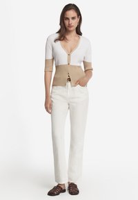 Virkat kavaj i vitt och beige med korta ärmar, V-ringning och knappstängning. Kombinerad med vita byxor och bruna sandaler med remmar.