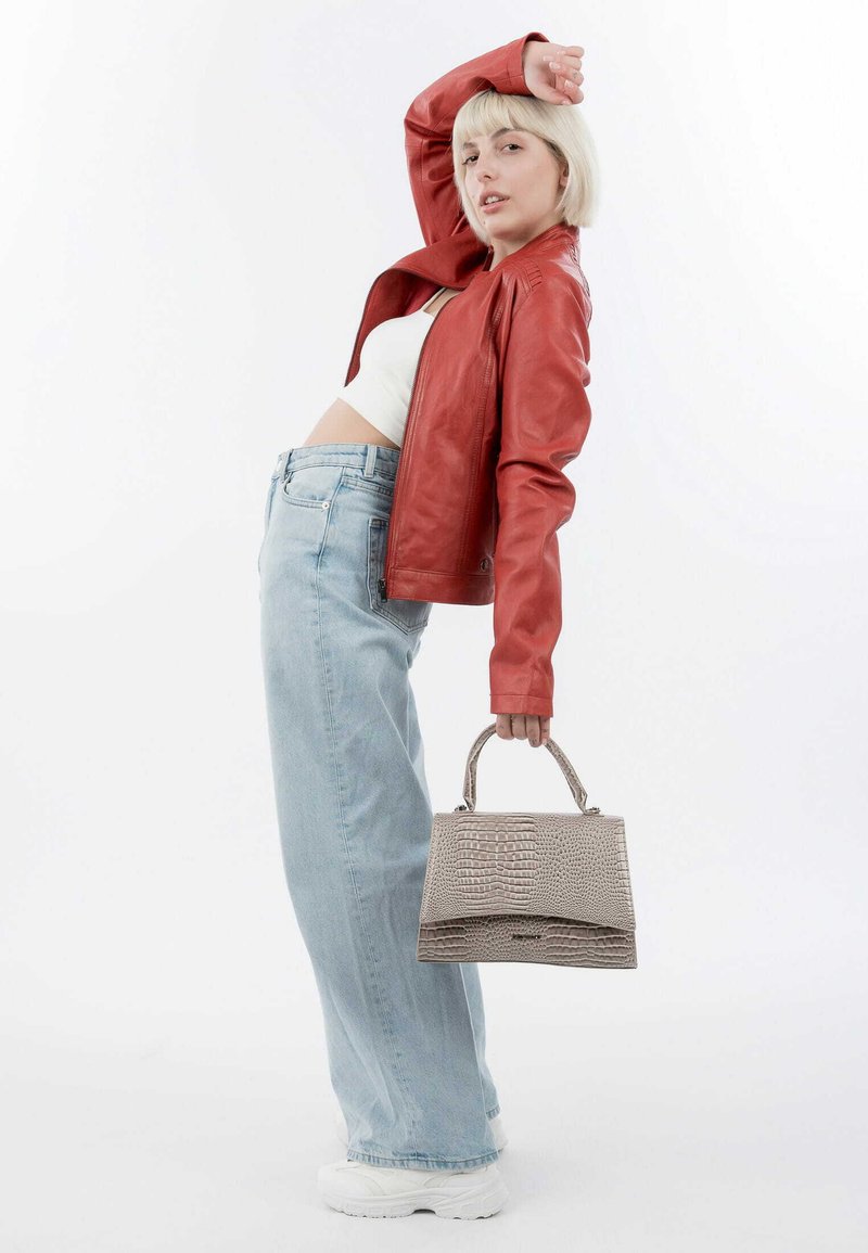 Rode leren jack, witte cropped top, lichtblauwe wijde jeans, grijze gestructureerde handtas met hengsels, witte sneakers, staande pose.
