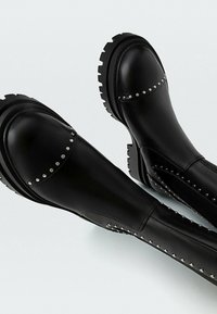 Bottes noires en cuir jusqu'à la cheville avec un bout arrondi, des accents cloutés sur les côtés, et une semelle texturée et robuste pour l'adhérence.