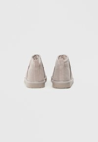 Botas de tornozelo em camurça de cor cinza claro com um forro de pele suave, sola de borracha plana e duas costuras verticais de cada lado, desenhadas para proporcionar conforto.