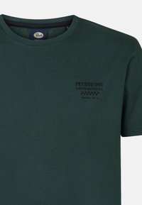 Tmavě zelené bavlněné tričko s kulatým výstřihem. Obsahuje černě potisknuté logo na levém hrudním prostoru a krátké rukávy.