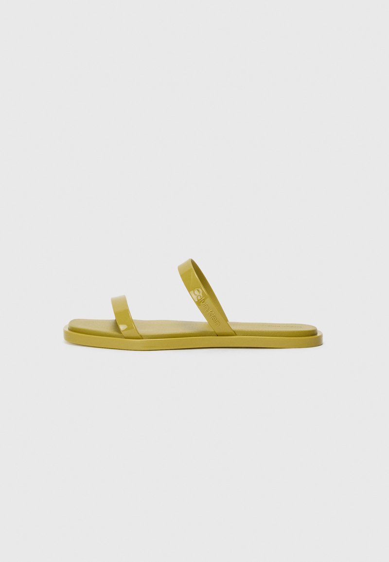 Flate, åpne sandaler i en dempet grønnfarge med to smale, blanke stropper; laget av et glatt, fleksibelt materiale. Logodetalj synlig.