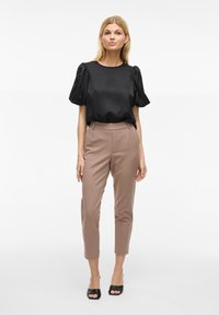 Top in satin nero con maniche a sbuffo, abbinato a pantaloni tailleur marrone chiaro e decolleté neri con apertura. Design semplice con texture lisce.