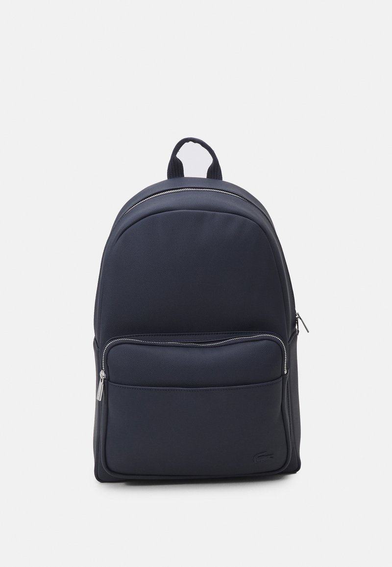 Mochila azul marinho feita de tecido texturizado com um bolso frontal liso, fechos de zíper duplos e uma alça de transporte superior. Design simples e estruturado.