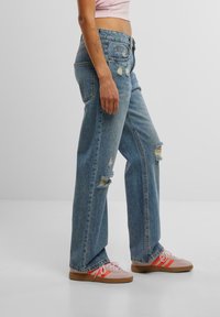 Light blue denim wide-leg jeans with frayed edges and distressed details on the legs, paired with pink sneakers featuring orange accents.
