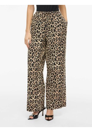 Spodnie z szerokimi nogawkami w beżowo-czarny wzór w cętki, z wiązanym w pasie sznurkiem, bocznymi kieszeniami, noszone z czarnymi sandałami na wysokim obcasie i otwartymi palcami.