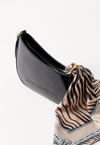 Μαύρη δερμάτινη τσάντα χειρός με καμπυλωτό σχήμα, με χρυσά αξεσουάρ και συνημμένο κασκόλ σε καφέ απόχρωση με σχέδιο λωρίδων τίγρης και λογότυπο.