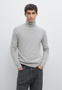 Maglione a collo alto grigio chiaro realizzato in morbido tessuto a maglia, con maniche lunghe e un design aderente, abbinato a jeans grigio scuro.