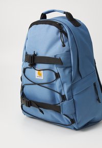Blauer Rucksack aus strapazierfähigem Gewebe mit schwarzen Trägern, Reißverschlüssen und einem Logo-Tag. Er hat ein strukturiertes Design und mehrere Befestigungspunkte.
