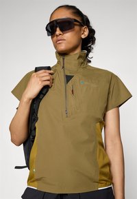 Lightweight, olive green performance top with short sleeves, a quarter zip, and mesh side panels, paired with sleek black sunglasses.